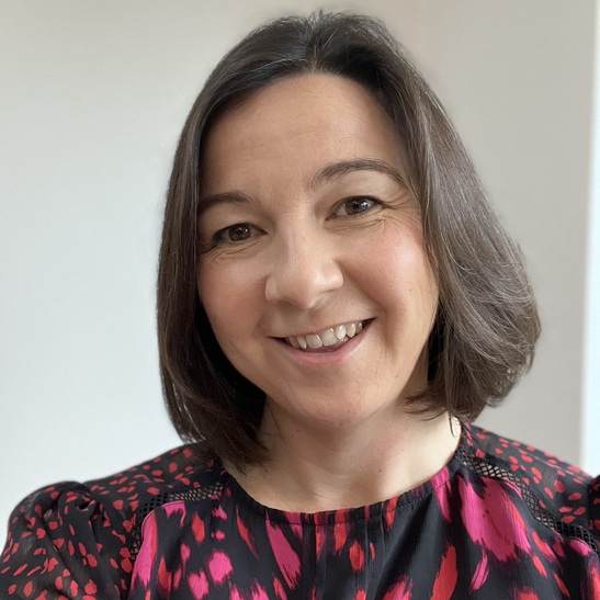 Dr Sophie West Profile picture smiling with a short brunette bon and high neck red and black dress